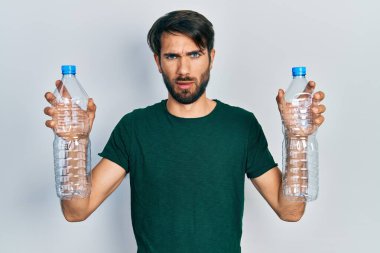 İspanyol asıllı genç adam plastik şişeleri şok yüzünden geri dönüşüm kutusunu tutuyor, şüpheci ve alaycı görünüyor, ağzı açık kalınca şaşırıyor. 