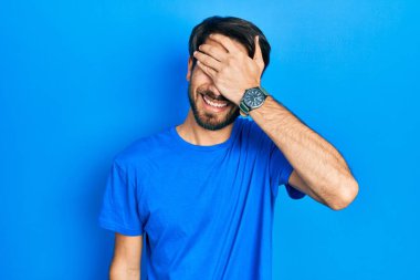 Gündelik kıyafetler giyen, gülümseyen ve gülümseyen genç İspanyol adam şaşırmak için gözlerini kapatıyor. kör kavram. 