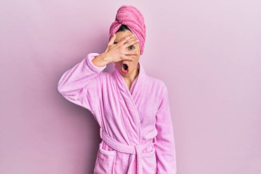 Duş başlığı ve bornoz takan genç sarışın kadın şok içinde yüzünü ve gözlerini kapayarak utangaç bir ifadeyle parmaklarından bakıyor.. 