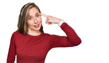 Sıradan kıyafetler giyen genç sarışın kadın gülümseyerek tek parmağıyla kafasını işaret ediyor, harika bir fikir ya da düşünce, iyi bir hafıza. 