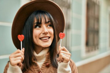 Kış şapkası takan esmer kadın şehirde lolipop tutuyor.