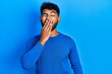 Sıradan mavi süveter giyen sakallı bir Arap, ağzıyla ağzını kapatmaktan sıkılmış. Huzursuz ve uykulu.. 