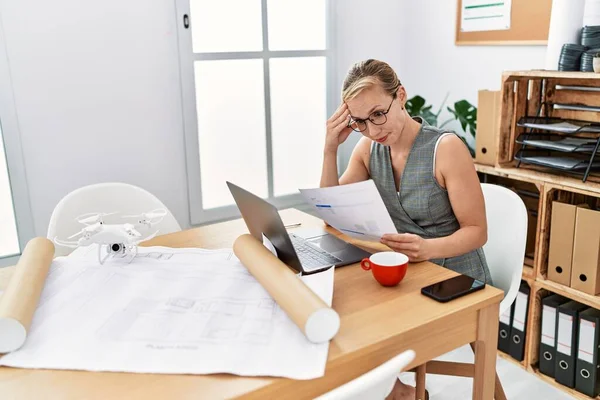 Genç beyaz kadın mimarlık stüdyosunda çalışan belgeleri okuyor.