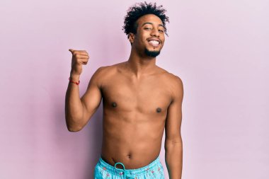 Sakallı, mutlu yüzüyle gülümseyen ve baş parmağıyla yüzünü gösteren Afro-Amerikan genç adam.. 