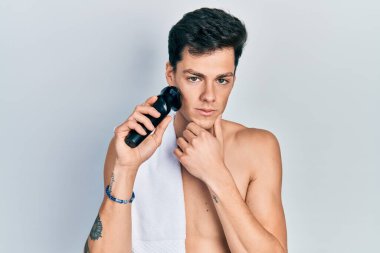 Elektrikli tıraş makinesiyle tıraş olan genç İspanyol adam şüpheci ve gergin, sorun yüzünden surat asıyor. negatif kişi. 