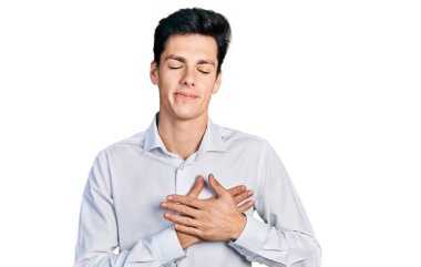 Genç İspanyol iş adamı iş kıyafetleri giyiyor, elleri göğsünde, gözleri kapalı gülümsüyor ve yüzünde minnet ifadesi var. sağlık kavramı. 