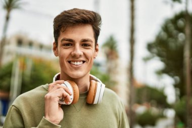 Şehirde kulaklık takarak mutlu gülümseyen genç İspanyol adam..