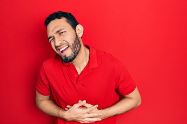 Sakallı İspanyol bir adam, elleri karnında, gündelik kırmızı tişört giyiyor çünkü mide bulantısı, acı verici bir hastalık kendini iyi hissetmiyor. Ağrı kavramı. 