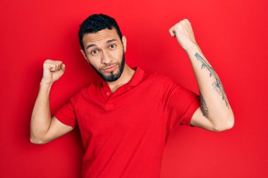 Sakallı, sıradan kırmızı tişörtlü İspanyol adam gururla gülümseyen kol kaslarını gösteriyor. fitness konsepti. 