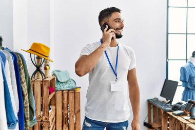 Genç Arap esnaf akıllı telefondan konuşuyor giyim mağazasında elbise rafının yanında duruyor.