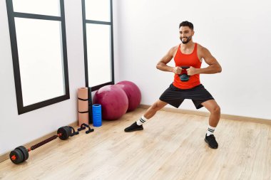 Genç Arap adam gülümsüyor spor merkezinde kettlebell ile antrenman yapıyor.
