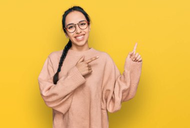 Gündelik kıyafetler giyen, gözlüklü, gülümseyen ve kameraya bakan genç İspanyol kız iki eliyle ve parmaklarıyla kenarı işaret ediyor.. 