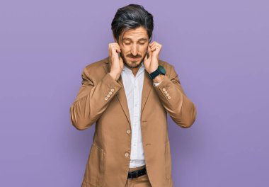 Genç İspanyol adam iş kıyafetleri giyip kulaklarını parmaklarıyla kapatıyor ve yüksek sesli müzik sesi için rahatsız edici bir ifade takınıyor. sağır kavramı. 