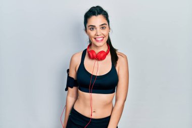 Spor kıyafetleri giyen ve kulaklık takan genç İspanyol kız kameraya seksi bir ifadeyle bakıyor, neşeli ve mutlu bir yüzle.. 