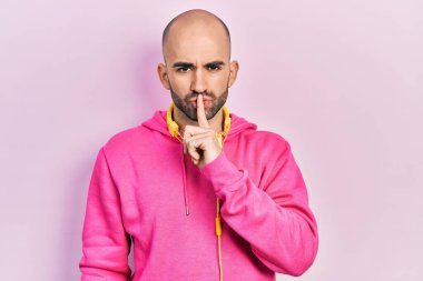 Spor kıyafetleri giyen ve kulaklık takan genç kel bir adam sessiz olmasını istiyor. sessizlik ve gizli konsept. 