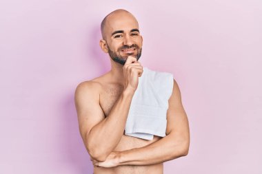 Tişörtsüz genç kel adam kameraya bakarak gülümsüyor. Kolları çapraz ve elleri çenesinde. Olumlu düşünmek. 