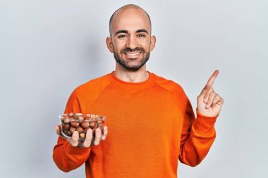 Çıplak fındık tutan genç kel adam gülümsüyor. 