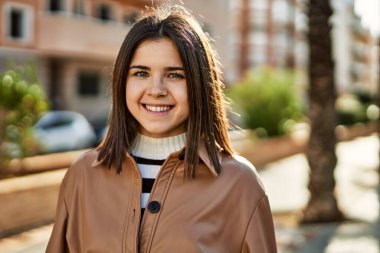 Genç, güzel, esmer kadın dışarıda mutlu bir şekilde gülümsüyor.