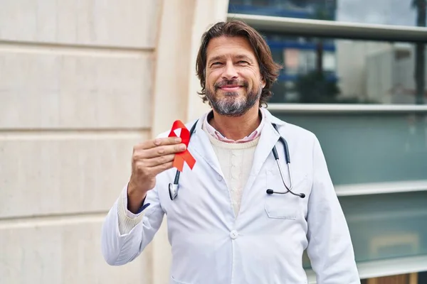 ハンサムな中年医師男保持サポート赤いリボン見て正と幸せな立ちと笑顔で自信を持って笑顔示す歯 — ストック写真