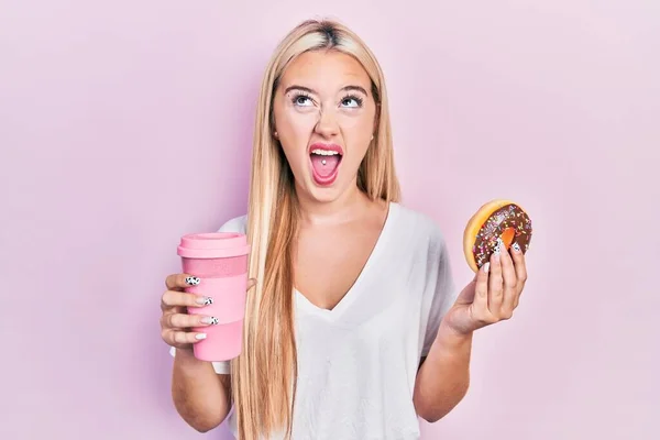 Jovem Loira Comendo Donut Bebendo Café Irritado Louco Gritando Frustrado — Fotografia de Stock