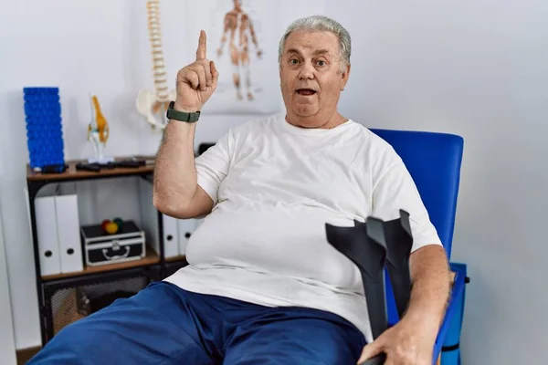 Hombre Caucásico Mayor Clínica Fisioterapia Sosteniendo Muletas Apuntando Con Dedo —  Fotos de Stock