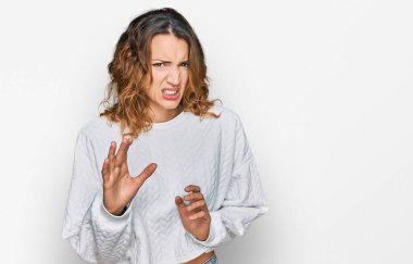 Beautiful young caucasian woman wearing casual winter sweater disgusted expression, displeased and fearful doing disgust face because aversion reaction. with hands raised  clipart