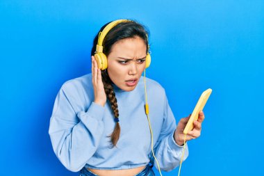 Genç İspanyol kız akıllı telefon ve kulaklık kullanıyor. Hiçbir şeyden haberi yok ve kafası karışık. şüphe kavramı. 