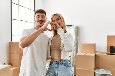 Genç beyaz çift gülümsüyor. Yeni evlerinde kalp sembolü yapıyorlar..