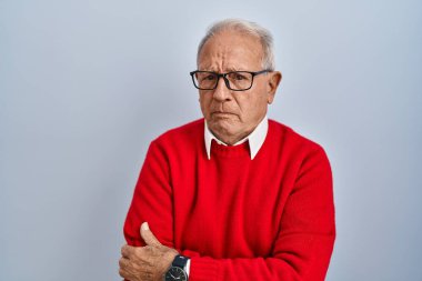 İzole edilmiş arka planda duran gri saçlı yaşlı adam şüpheci ve gergin, yüzünde çapraz kollu tasvip etmeyen ifade. negatif kişi. 