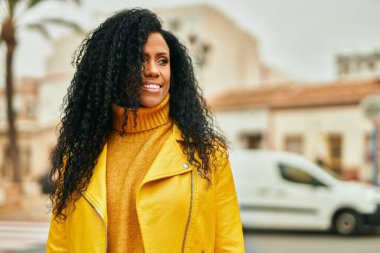 Orta yaşlı Afro-Amerikan kadın gülümseyerek şehirde mutlu mesut duruyor..