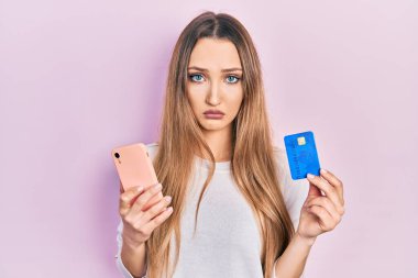 Akıllı telefon ve kredi kartı tutan genç sarışın kız sıkıntılı ve endişeli, sinirli ve korkmuş. hüzünlü ifade. 