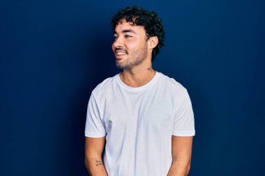 Gündelik beyaz tişört giyen genç İspanyol adam yüzünde gülümseme, doğal bir ifade ile yan yana bakıyor. Kendinden emin gülen. 