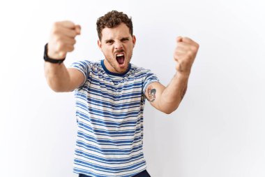 Tecrit edilmiş arka planda duran yakışıklı genç adam öfkeyle bağırırken kızgın ve kızgın yumruklar sallıyor. öfke ve agresif konsept. 