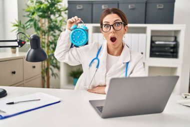 Genç esmer kadın alarmlı saati tutuyor. Şaşırmak için ağzı açık kalmış, korkmuş ve şaşkın. İnanmayan yüz. 