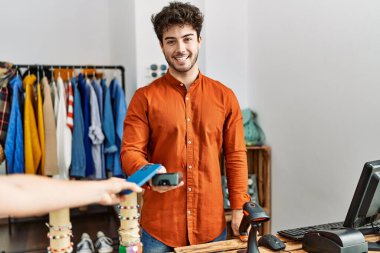 Customer hand paying to shopkeeper man using smartphone at clothing store.