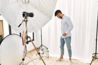 Arab young man posing as model at photography studio suffering of backache, touching back with hand, muscular pain 