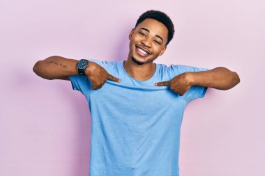 Genç, Afro-Amerikan bir adam, günlük mavi tişört giyiyor. Kendine güvenen, yüzünde gülümseme olan, kendini gururlu ve mutlu bir şekilde gösteren.. 