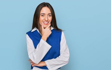 Gündelik kıyafetler giyen genç İspanyol kız kameraya kendinden emin bakıyor kollarını kavuşturup gülümsüyor ve çenesini kaldırıyor. Olumlu düşünmek. 