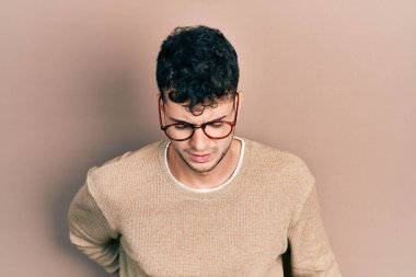 Sırt ağrısı çeken, sıradan kıyafetler ve gözlük takan İspanyol genç adam, elleriyle dokunuyor, kas ağrısı çekiyor. 