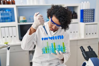 Laboratuvarda pipeti kullanan, bilim adamı üniforması giyen genç bir İspanyol.