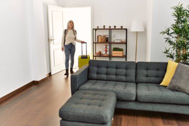 Orta yaşlı, gri saçlı, sırt çantalı bir turist. Elinde bavulla eve gidiyor.