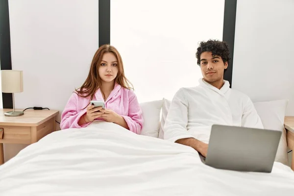 Pareja Joven Con Expresión Seria Usando Laptop Smartphone Dormitorio — Foto de Stock