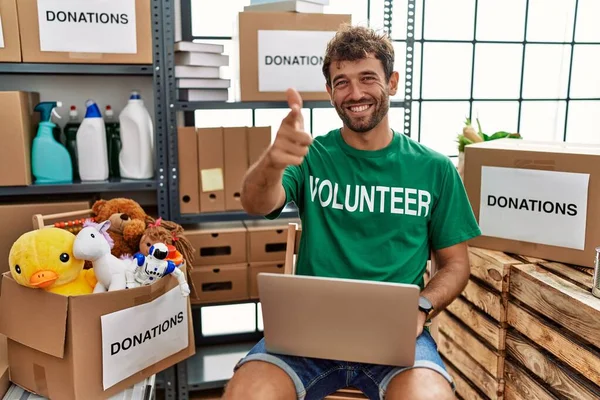 年轻英俊的男子穿着志愿者的T恤 用手提电脑指尖镜头 脸上带着快乐和滑稽的表情 充沛的精力和活力 — 图库照片