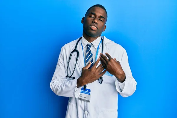 Young African American Man Wearing Doctor Uniform Smiling Hands Chest — стоковое фото