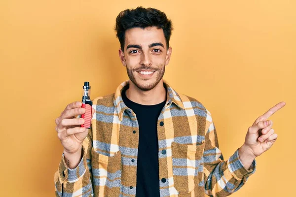 Ung Latinamerikansk Man Som Håller Elektronisk Cigarett Leende Glad Pekar — Stockfoto
