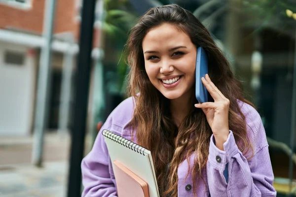 Young hispanic student woman smiling happy talking on the smartphone at the city.
