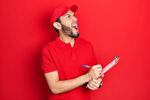 Homem Hispânico Com Barba Vestindo Uniforme Mensageiro Segurando Prancheta Irritado — Fotografia de Stock