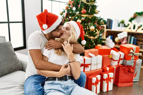 Young Couple Kissing Wearing Christmas Hugging Sitting Sofa Hat Home — Stock Photo, Image