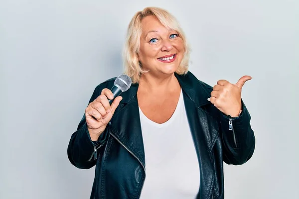 Middle Age Blonde Woman Singing Song Using Microphone Pointing Thumb — Stock Photo, Image