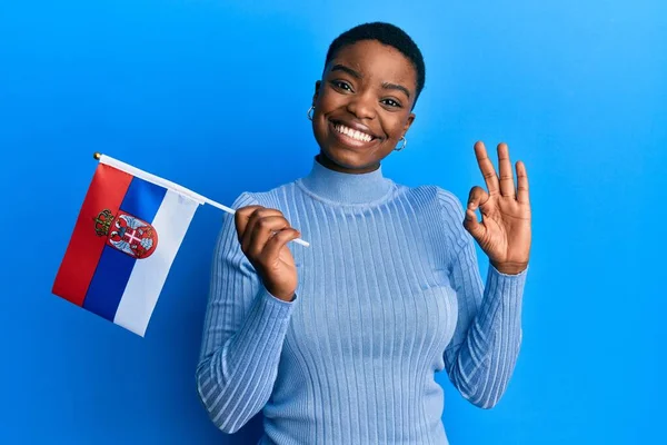 Young African American Woman Holding Serbia Flag Doing Sign Fingers — Stockfoto